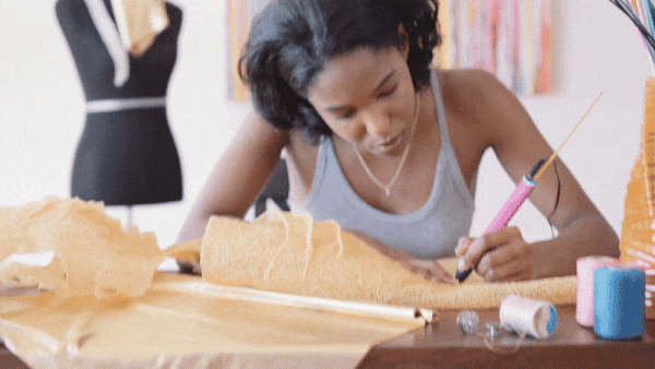 Woman crafting fabric with 3D pen strands.