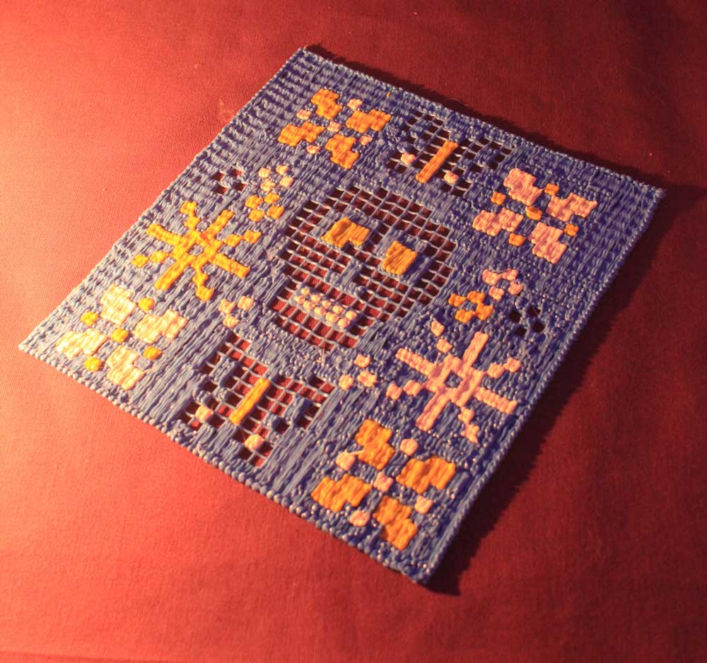 Blue & yellow cross-stitched 3D pen placemat on red table.